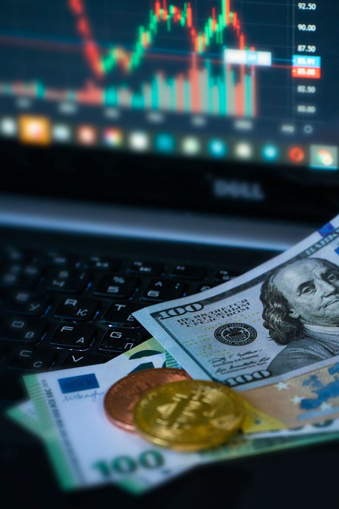Golden bitcoins and various banknotes in front of a financial chart on a laptop.